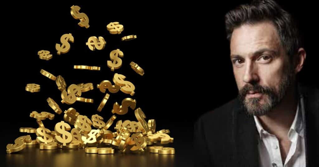 A man with a beard gazes thoughtfully at a gold coin, symbolizing wealth and reflection.