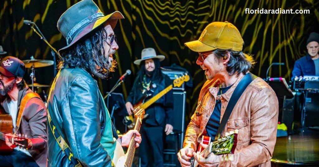 Two men wearing hats perform on stage, playing guitars and engaging the audience with their music.